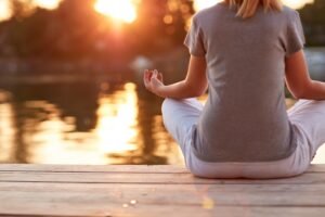 A woman meditates in a lotus position on a dock at sunset, reflecting tranquility and mindfulness.