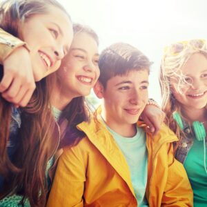 Four teenagers smiling and sitting close together outdoors, enjoying each other's company on a sunny day.