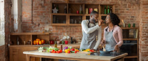 A couple joyfully cooking together in a modern kitchen, showcasing healthy ingredients like fresh vegetables, highlighting the importance of wellness and health checks.