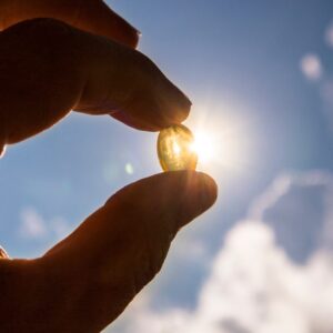 A hand holding a Vitamin D capsule against the bright sun, symbolizing the connection between sunlight and Vitamin D.