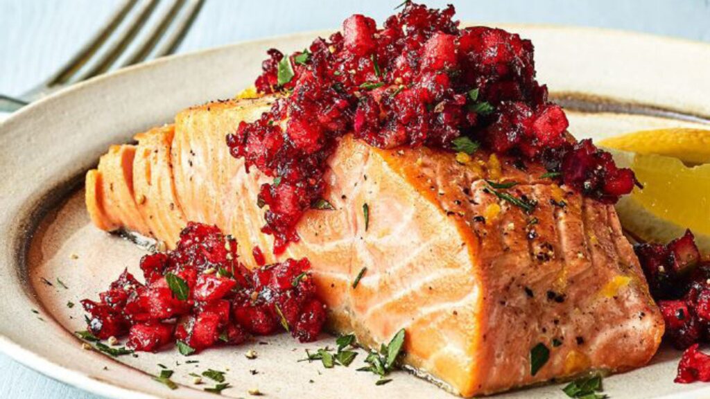 Roasted salmon fillet topped with spicy cranberry relish, garnished with fresh herbs and served with lemon wedges.