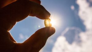 A hand holding a Vitamin D capsule against the bright sun, symbolizing the connection between sunlight and Vitamin D.